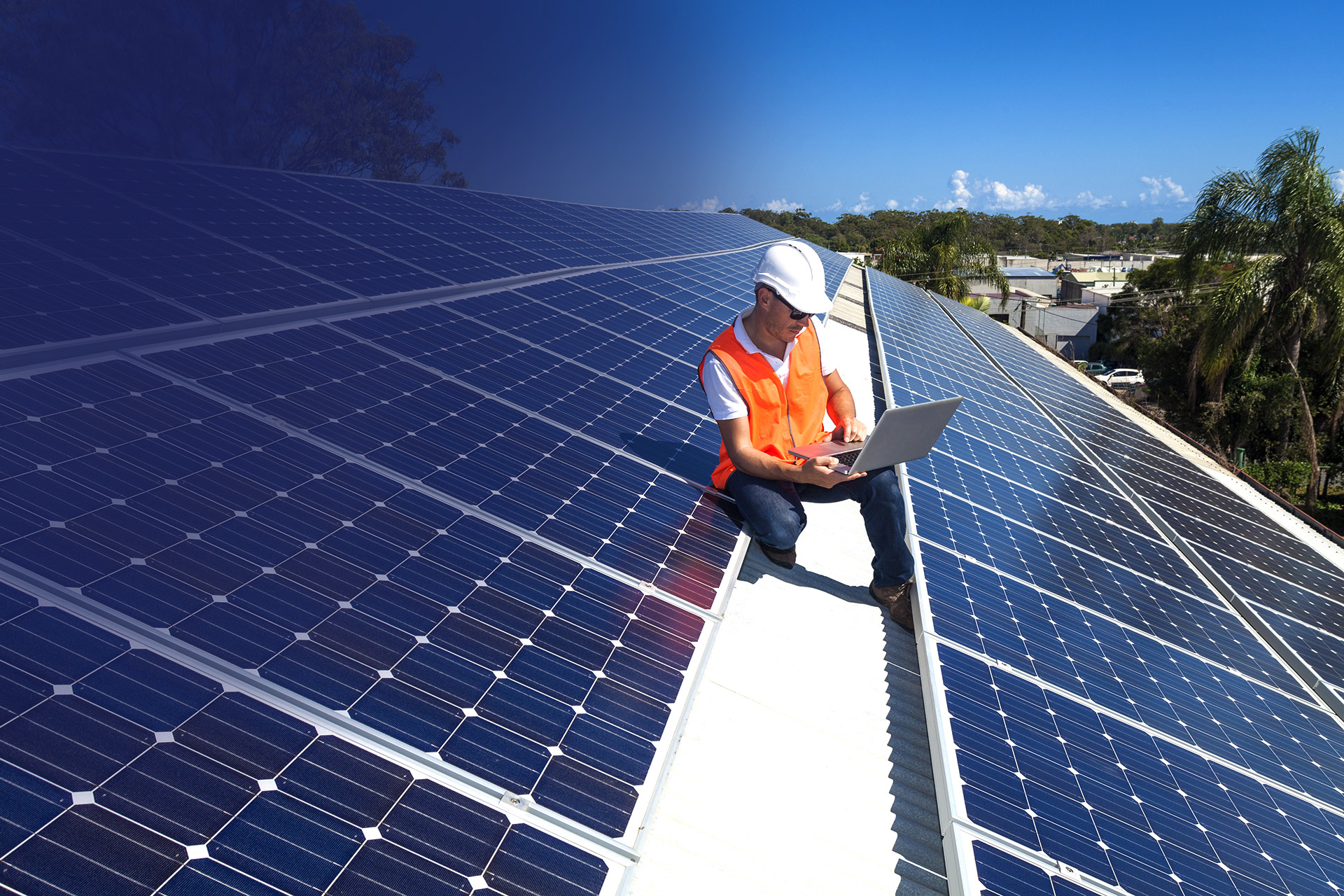Man installing solar panels on a roof with trees and buildings in background